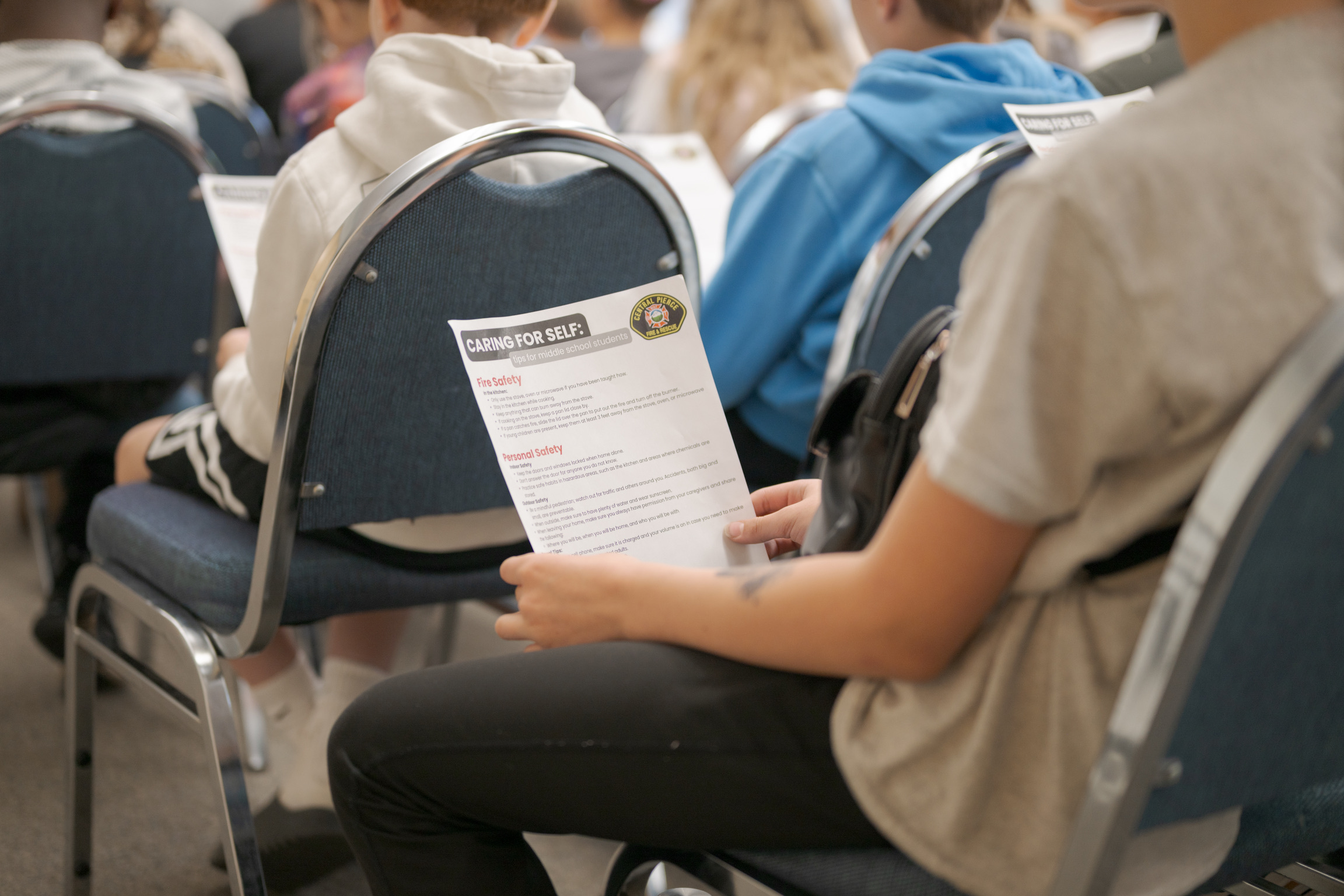A person seated among others holds a printed handout titled 