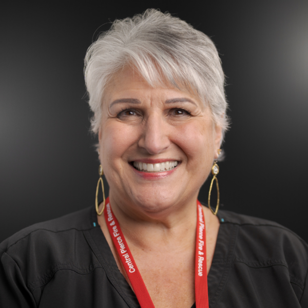 Smiling woman with short gray hair wearing a black top, long earrings, and a red lanyard that reads 