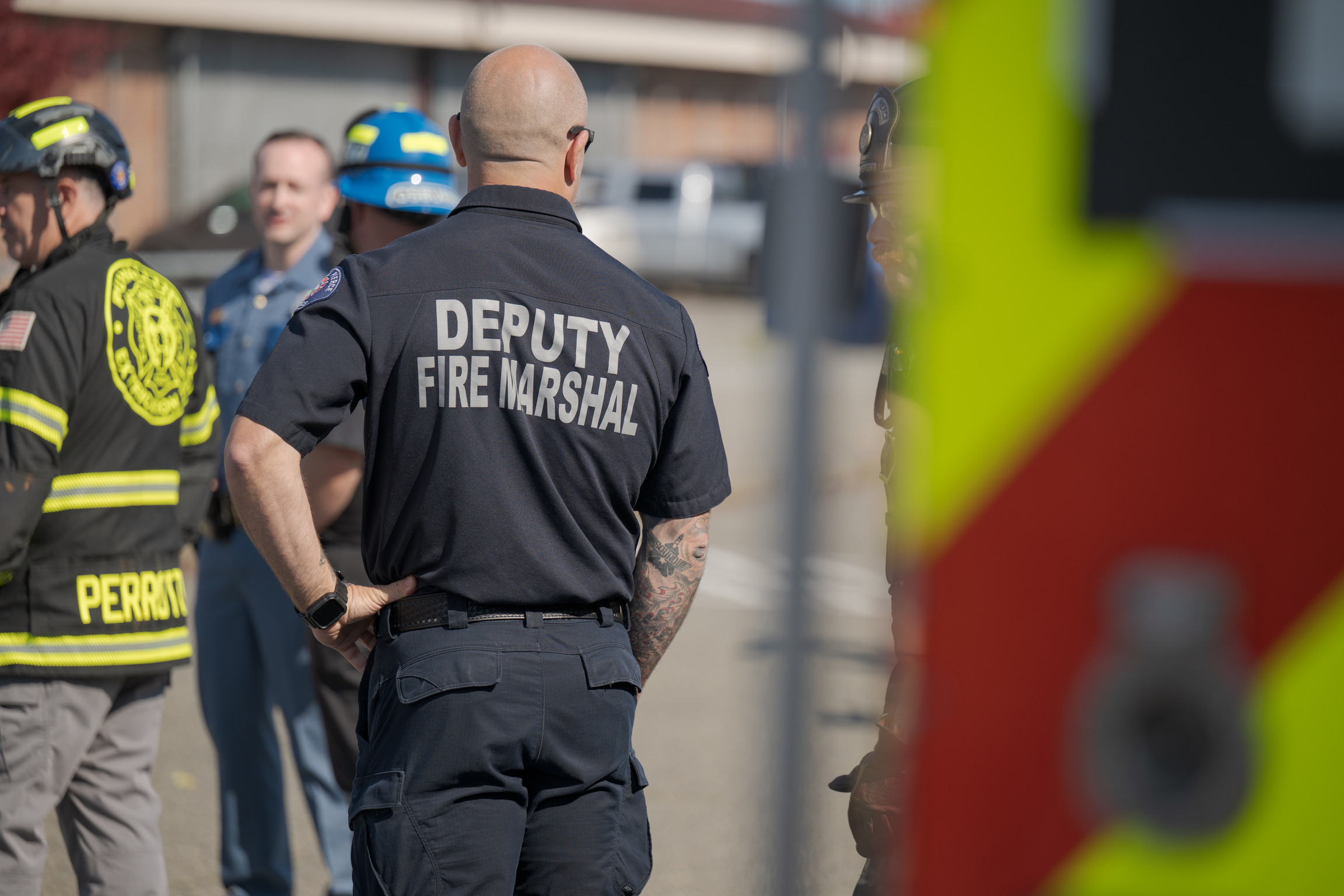 A group of emergency personnel, including a Central Pierce Fire Marshal, stand together outdoors near emergency vehicles.