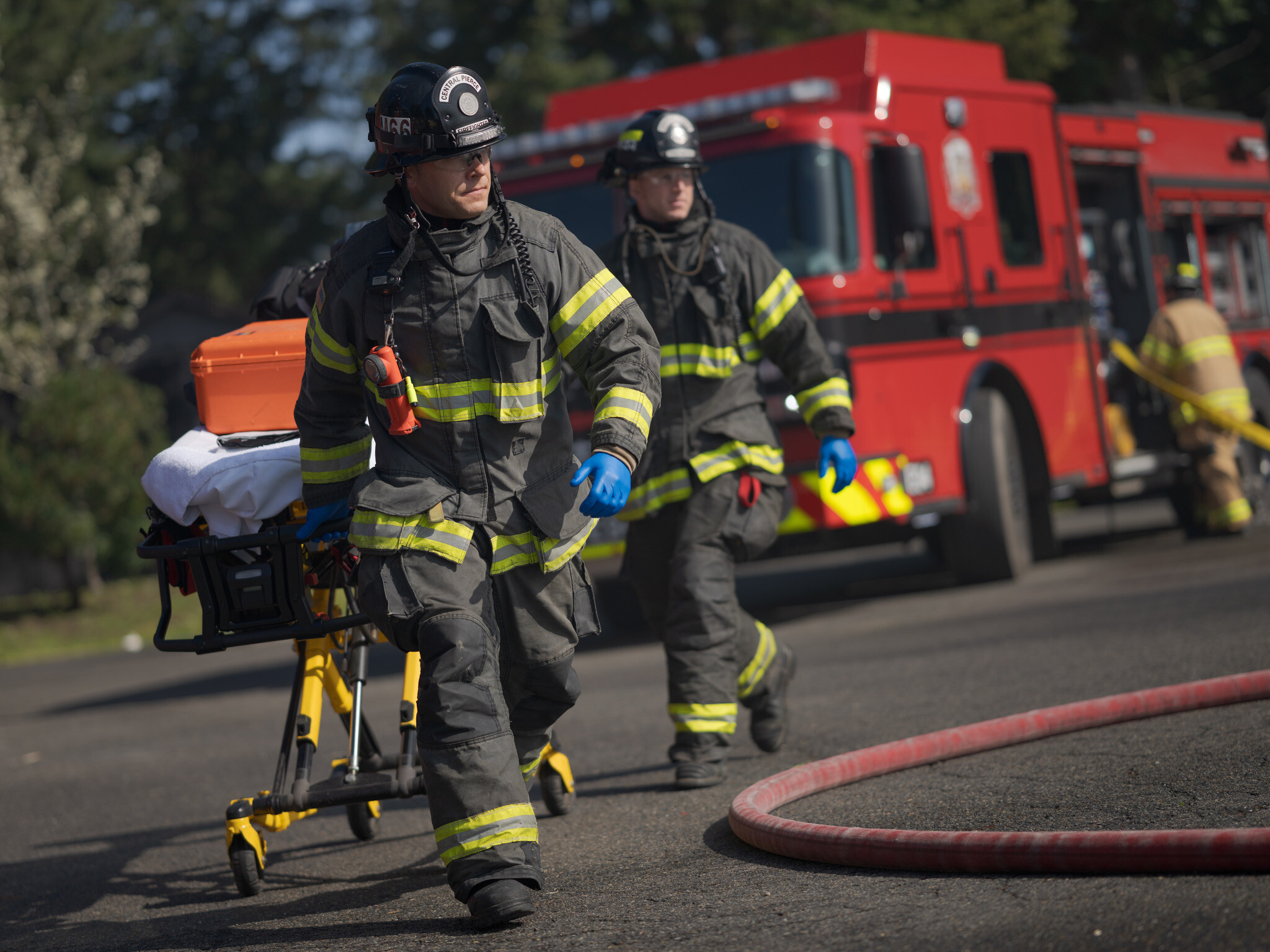 Two firefighters in full gear move a stretcher beside a Central Pierce Fire & Rescue truck, with another firefighter and fire hoses in the background&mdash;a scene typical during Ride-Along Requests.