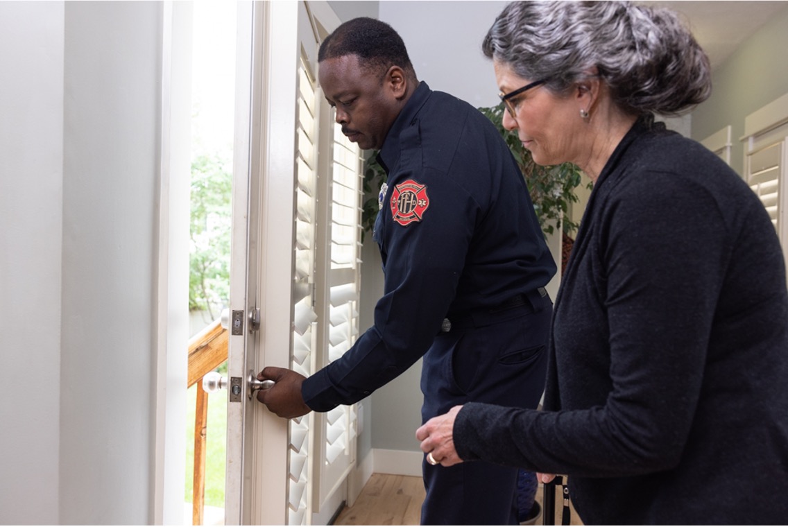 A firefighter in uniform helps a woman unlock a front door inside a house during daylight, demonstrating CPFR safety for older adults and supporting fall prevention for older adults in the community.