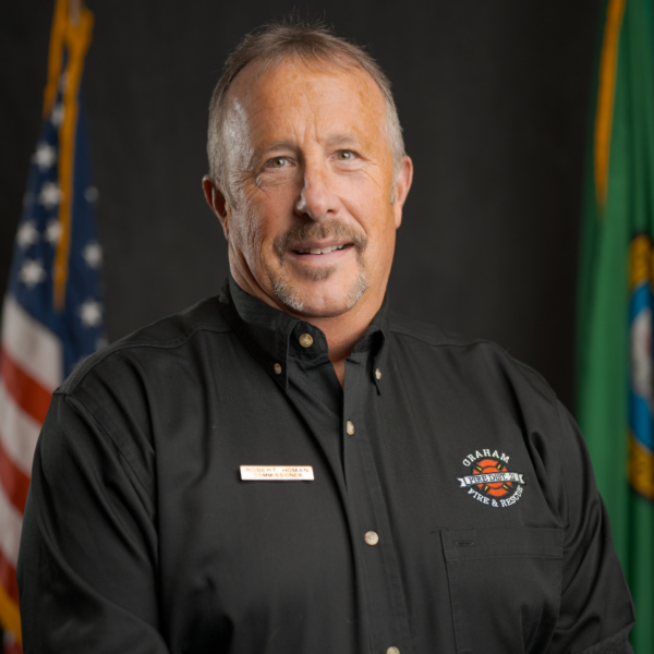 A middle-aged man in a black Graham Fire & Rescue shirt poses in front of American and Washington state flags.