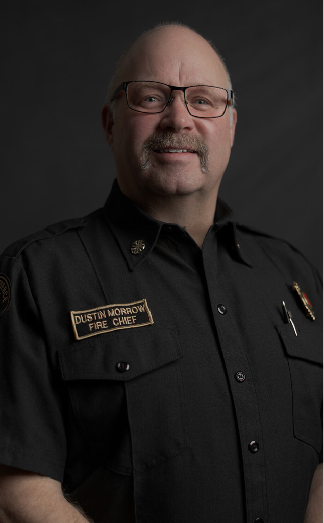 A man in a black fire chief uniform with a name tag reading 