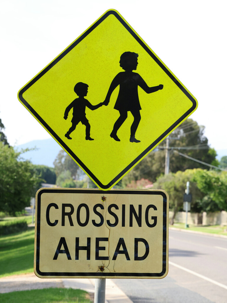Yellow road sign with silhouettes of a woman and child holding hands above a rectangular sign that reads 