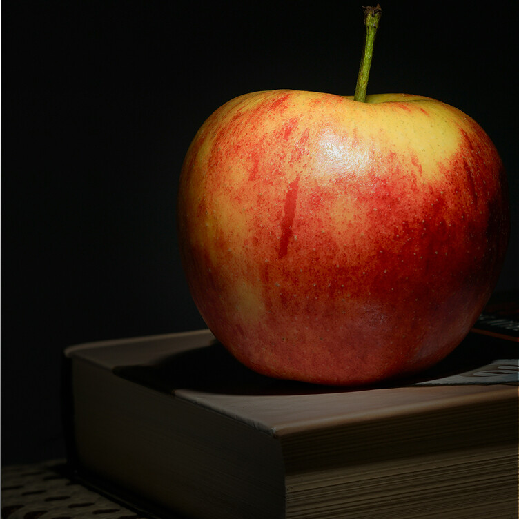 A red and yellow apple sits on top of a closed book, illuminated against a dark background.