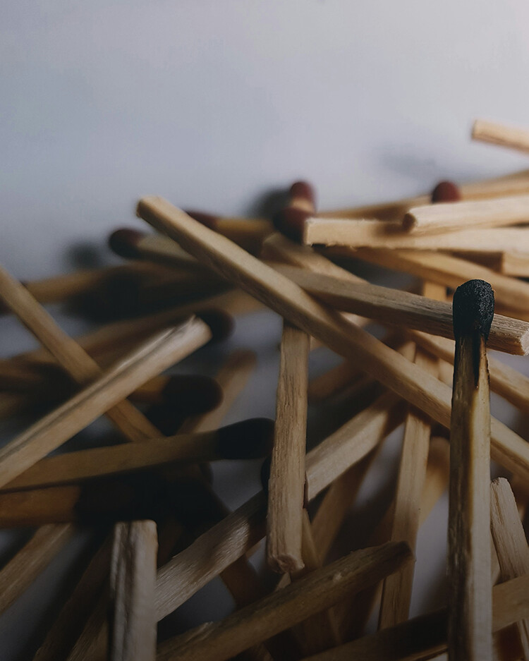 A pile of wooden matches, with one match in the foreground showing a burnt black tip.