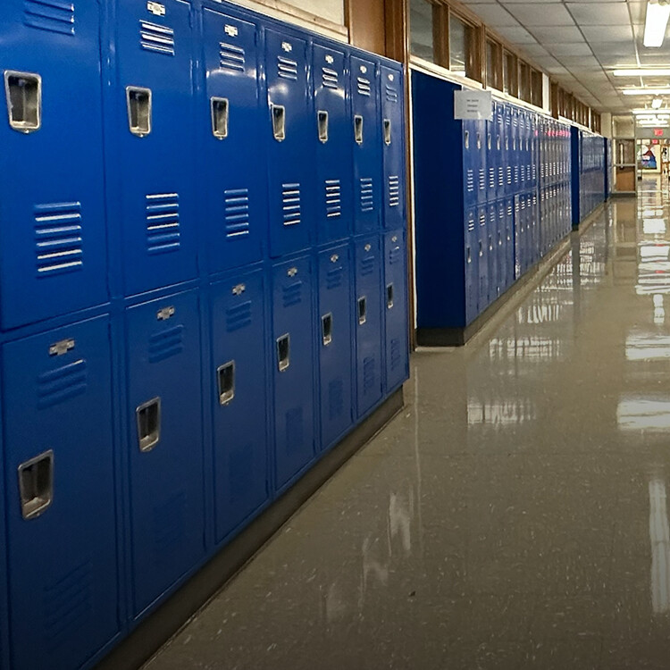 A hallway lined with closed blue lockers and reflective floors in a school building.