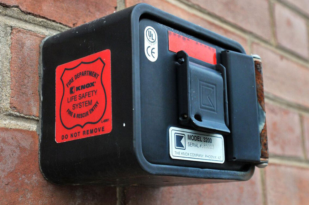 A black Knox Box, model 3200, is mounted on a brick wall with a red fire department life safety system sticker and certification labels from the Central Pierce Fire & Rescue Fire Marshal&rsquo;s Office.
