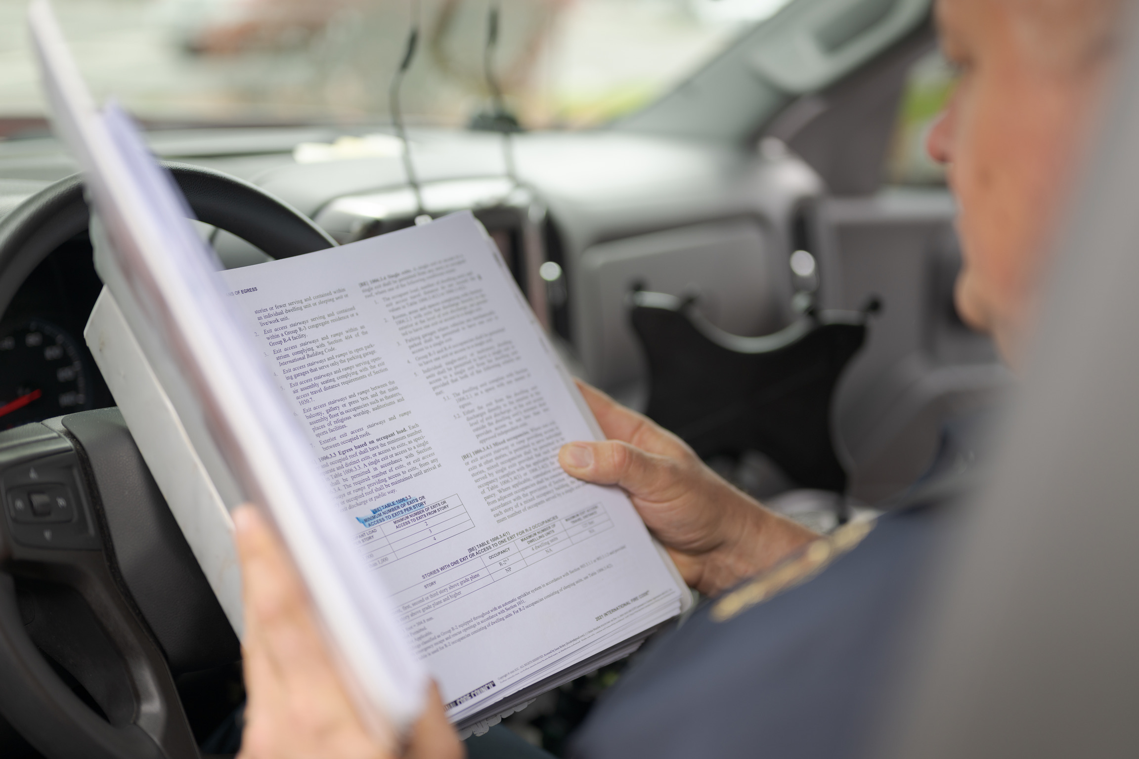 A person sitting in a vehicle reads a printed document with highlighted text and notes from the Central Pierce Fire & Rescue Fire Marshal&rsquo;s Office.