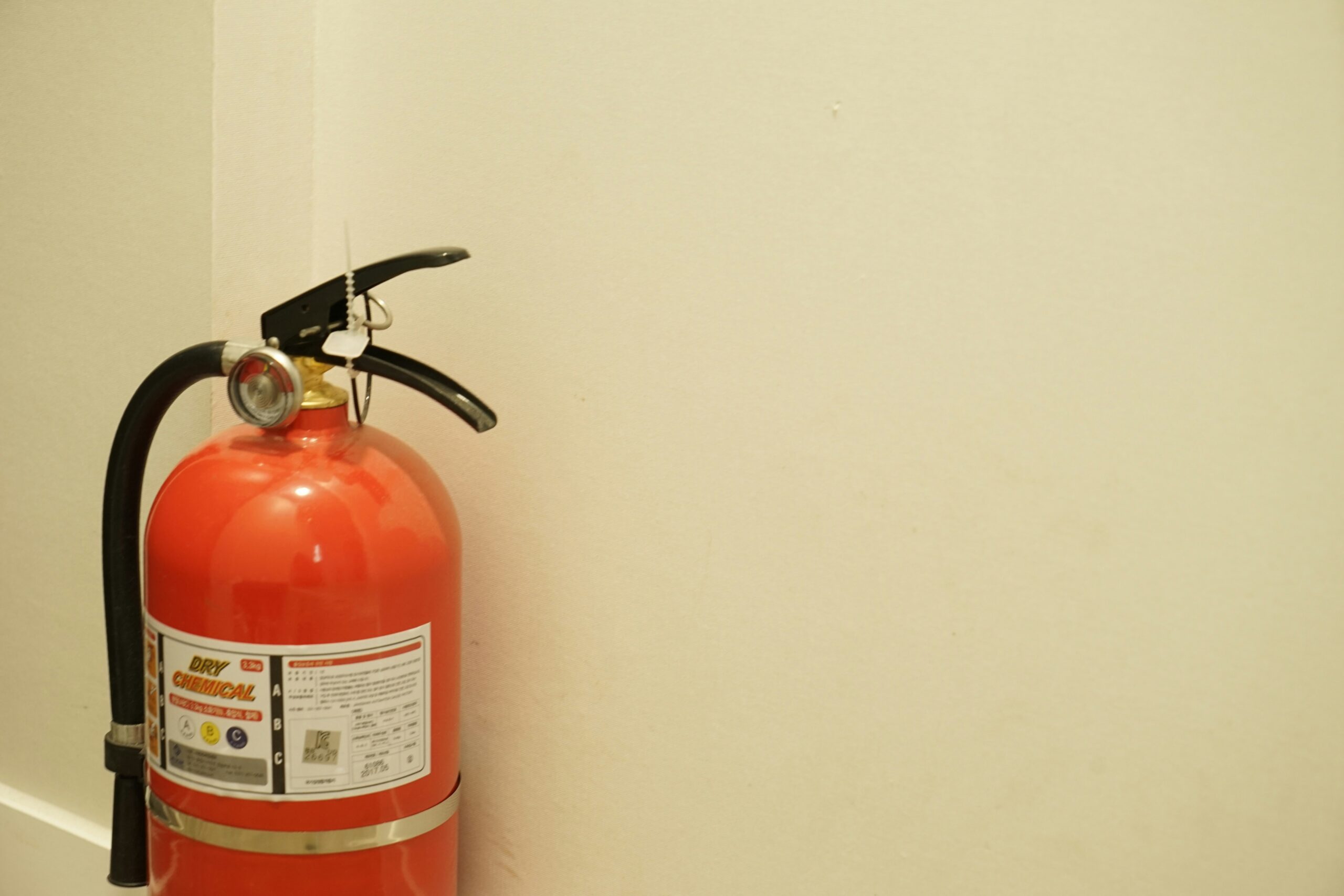 A red dry chemical fire extinguisher is placed against a white wall in the corner, emphasizing the importance of CPFR fire extinguisher classes for safety and preparedness.