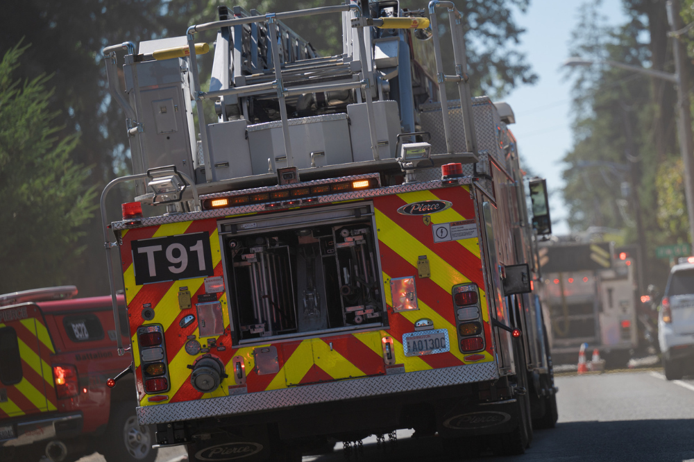 A Central Pierce Fire & Rescue ladder truck responding down a tree-lined road, with other emergency vehicles visible ahead and parked along the street.