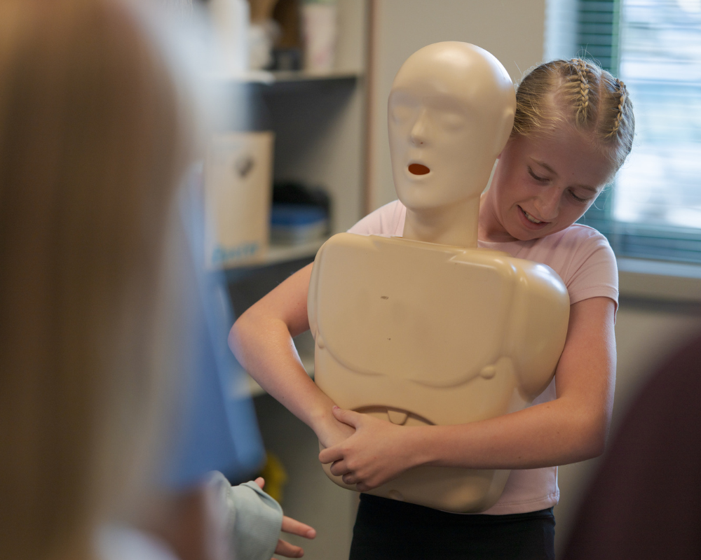 A girl practices the Heimlich maneuver on a CPR training dummy in a classroom setting during a Central Pierce Fire & Rescue Safe Sitter class.