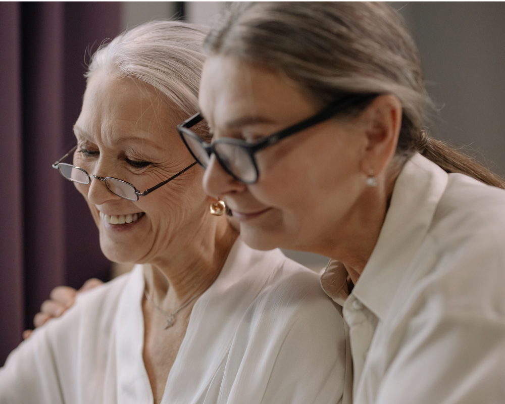 Two older women with gray hair and glasses sit close together, smiling as they look down—demonstrating CPFR safety for older adults and fall prevention awareness.