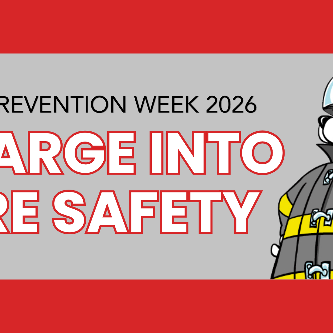 A cartoon fire dog in uniform stands next to the words “Fire Prevention Week 2026: Charge Into Fire Safety” on a red and gray background.